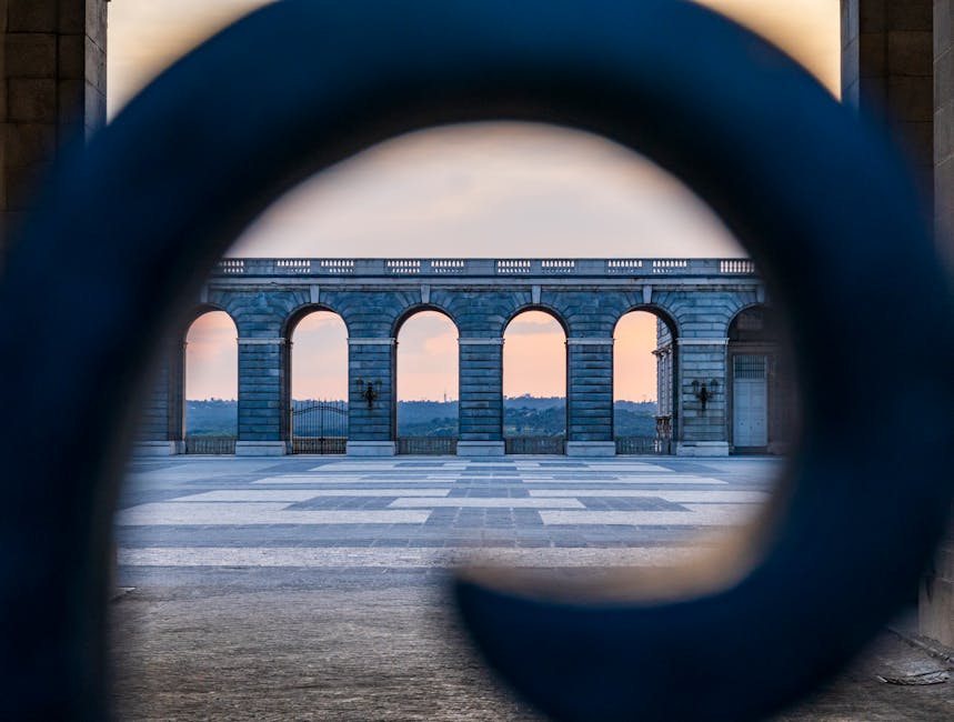 Beautiful view through ornate ironwork towards historic archway at sunset.