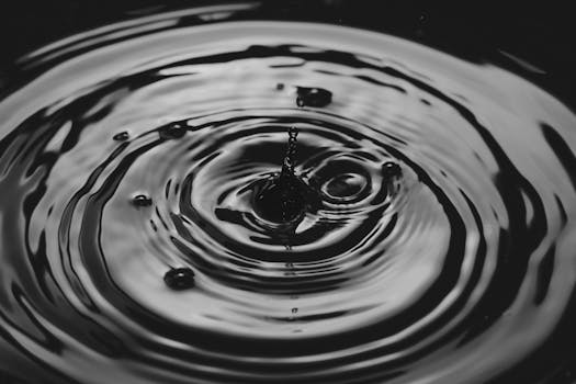 Artistic black and white close-up of a water droplet creating ripples, showcasing fluid dynamics.