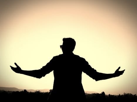 Silhouette of a man with open arms against a vibrant sunset background, symbolizing freedom and peace.